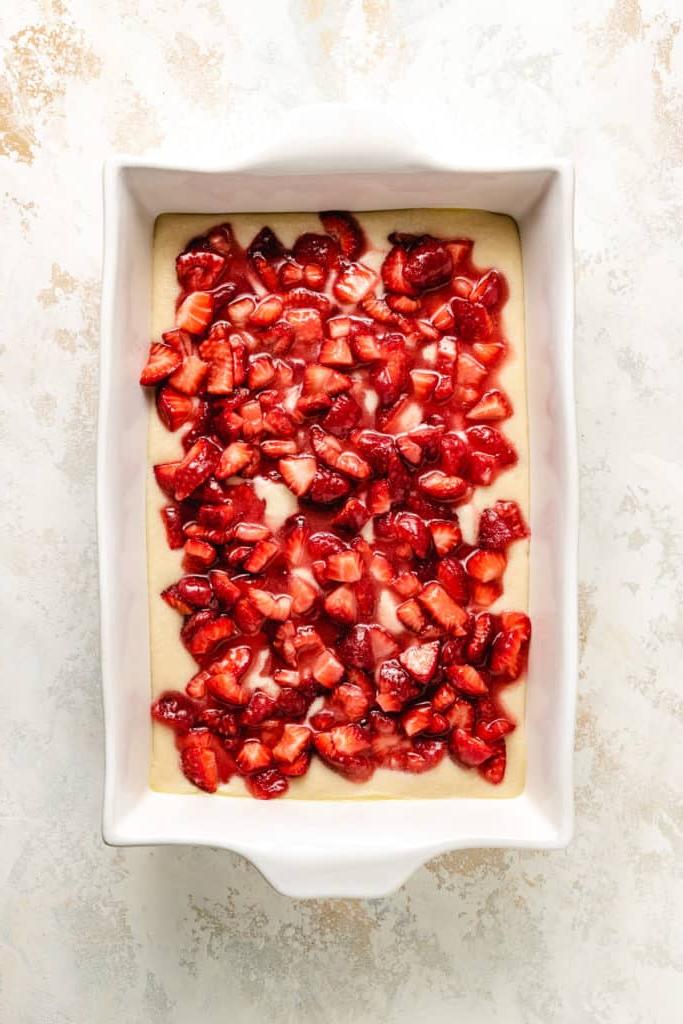 Strawberries layered over cobbler batter in a dish.