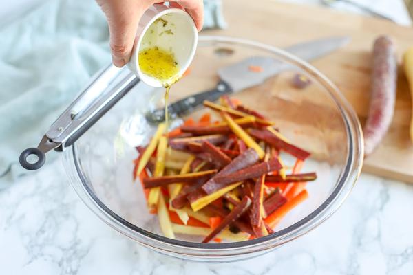 sliced carrots in a glass bowl with oil and herbs being poured on top
