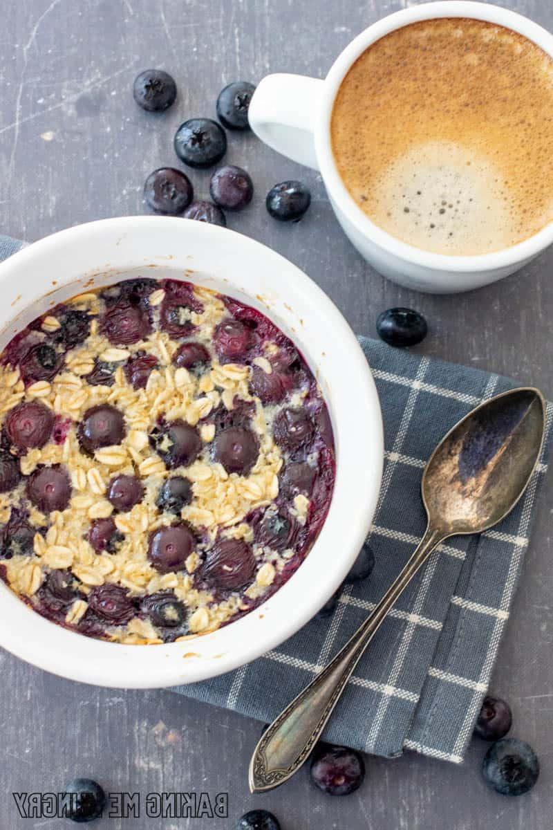 baked oats for one in a bowl with blueberries with a cup of espresso behind