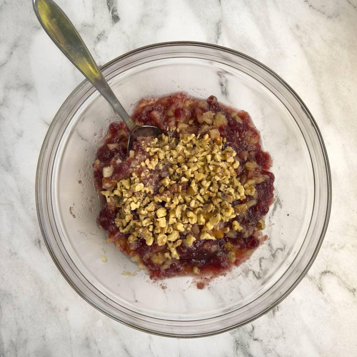 Fruit for a cranberry salad combined with chopped walnuts in a glass bowl.