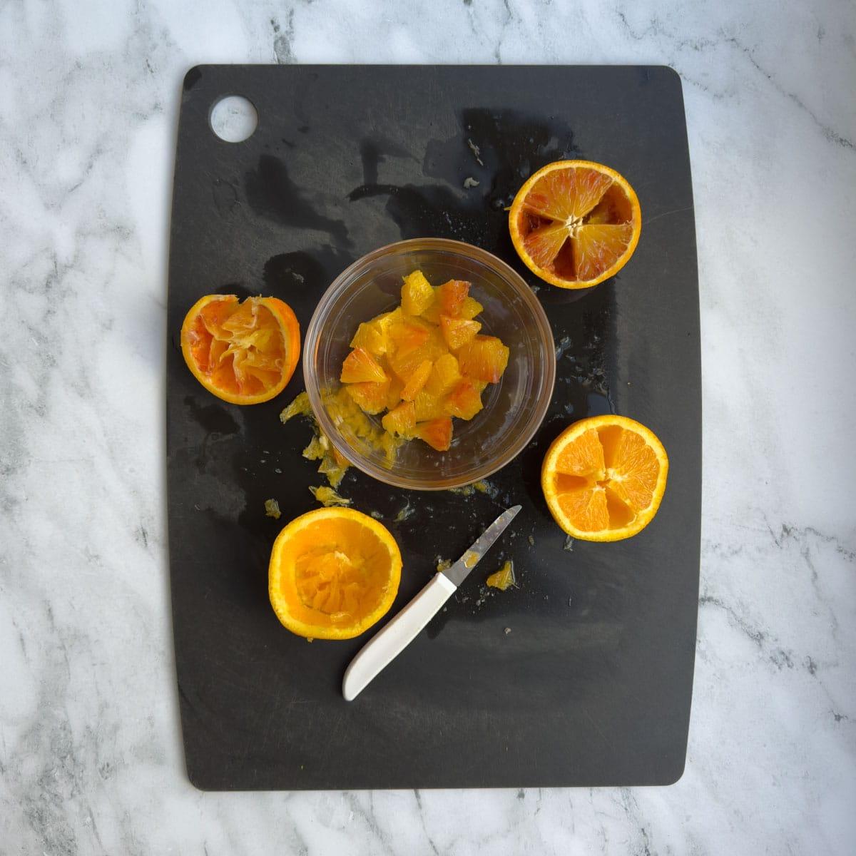 Cutting orange segments from oranges with a paring knife.