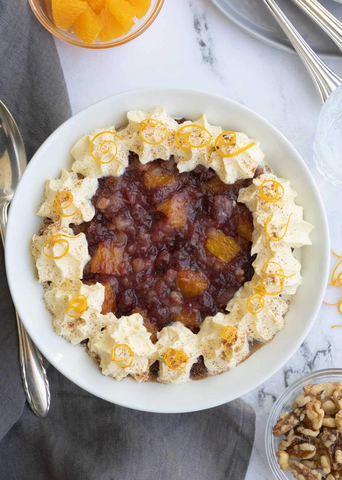 A cranberry, orange, pineapple and walnut salad in a white bowl with a silver spoon.