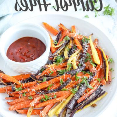 colorful baked carrot fries sprinkled with parsley and cheese on a white plate with ketchup