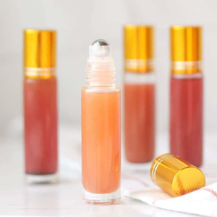 a pink lip gloss in a roller ball bottle with several bottles in the background