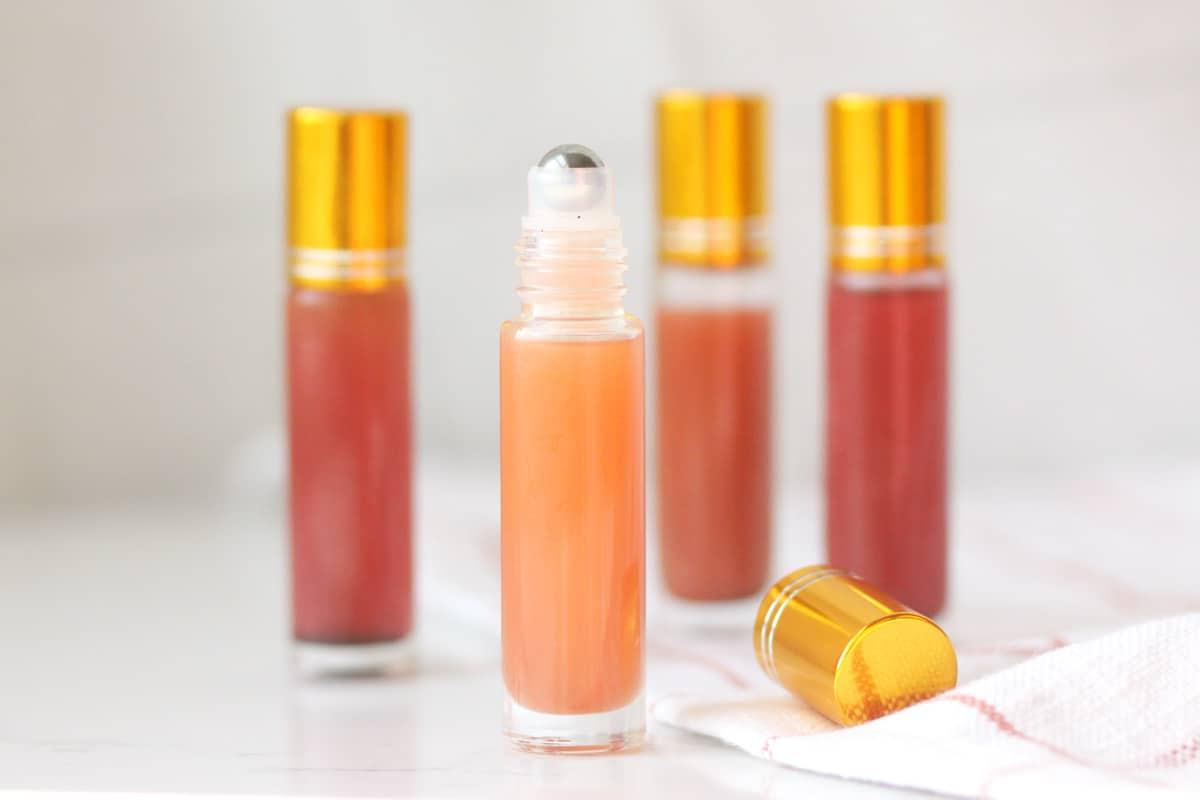 a pink lip gloss in a roller ball bottle with several bottles in the background