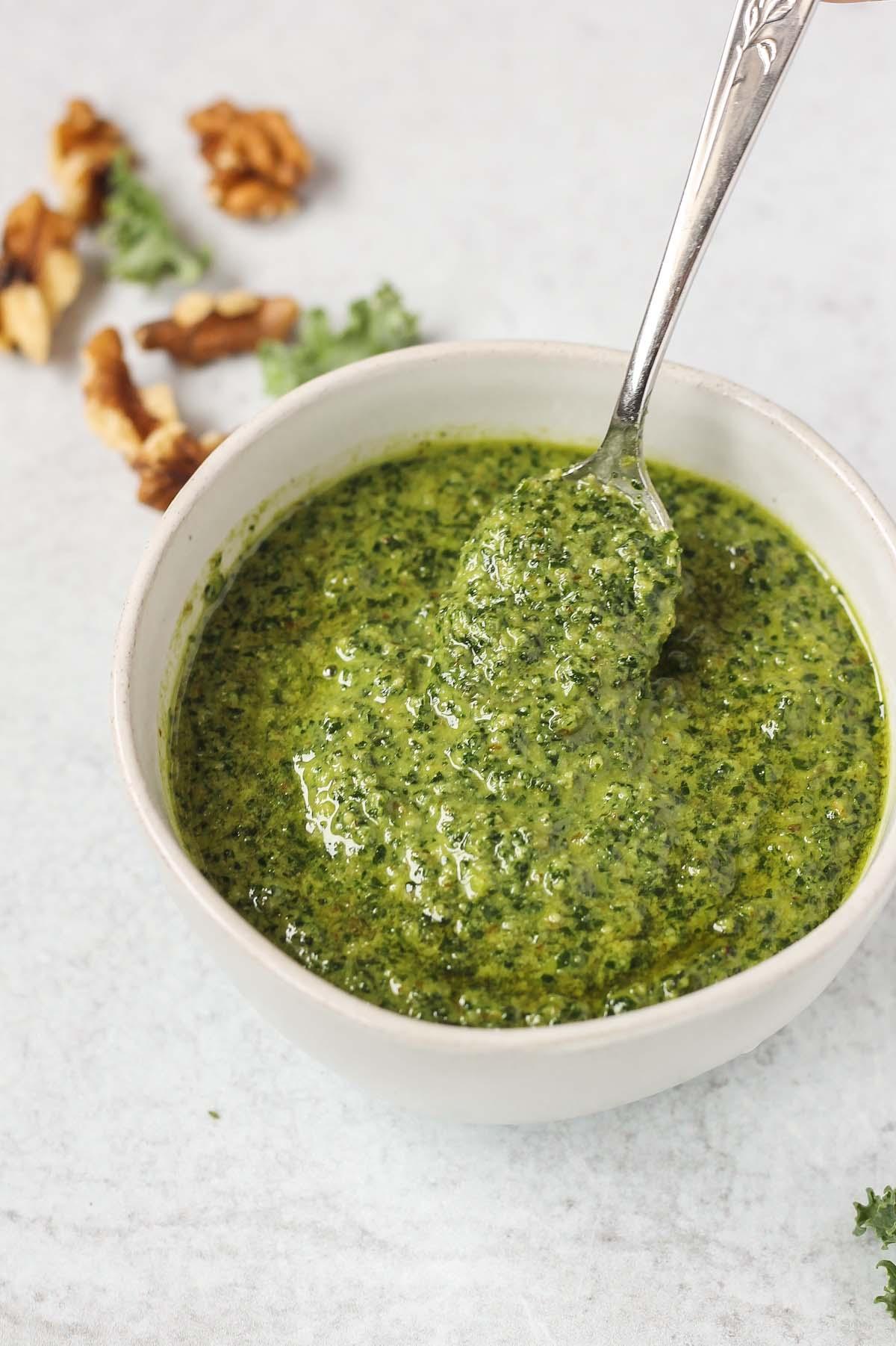 spoon scooping pesto from a small white bowl
