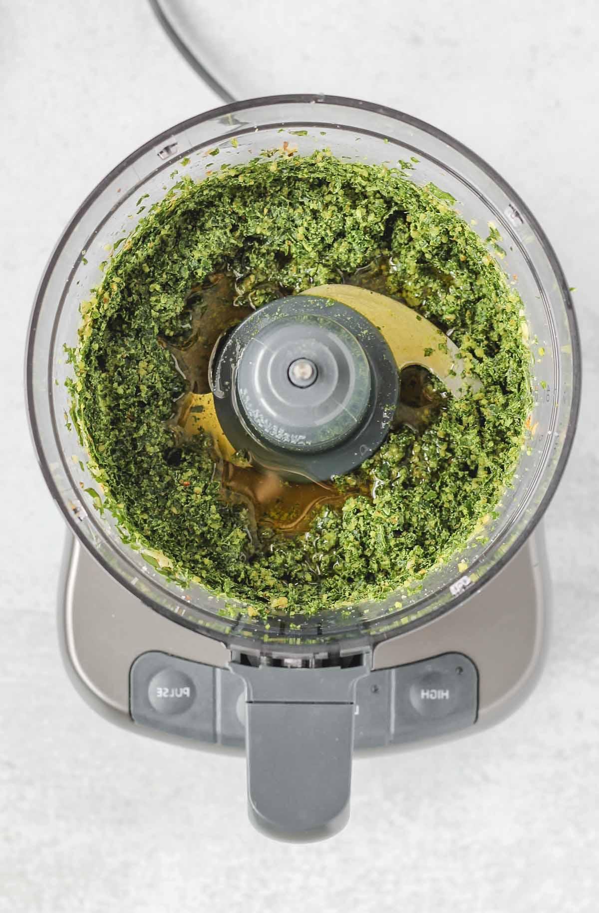 food processor with blended pesto ingredients and olive oil
