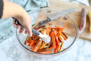 tossing oil into sliced carrots in a glass bowl